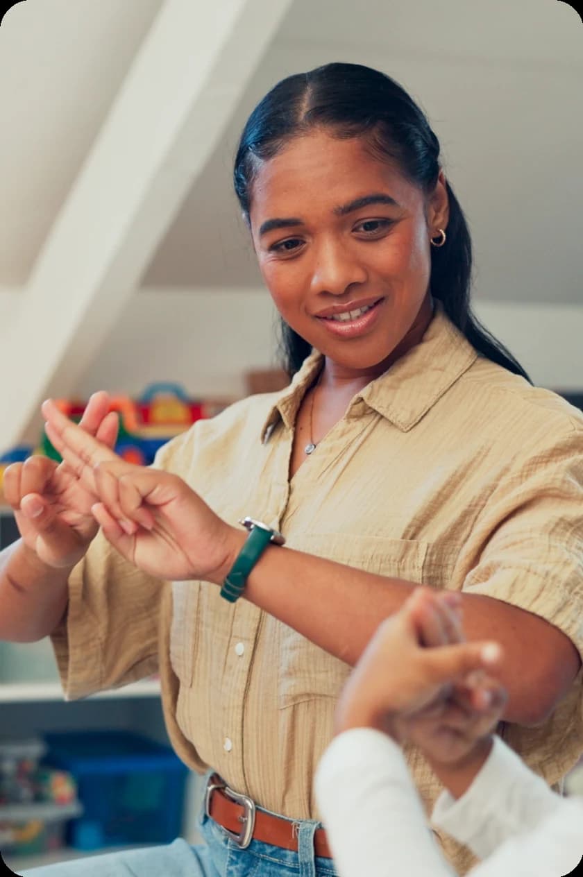 Ein Kind, das in der Schule mit seiner Lehrerin Gebärdensprache übt, und eine Mitarbeiterin, die Gebärdensprache bei der Arbeit übt